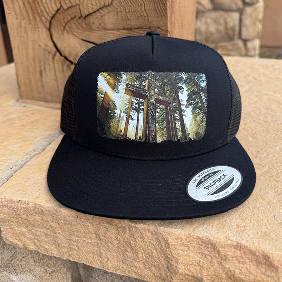 Black trucker cap with a forest design on a wooden surface