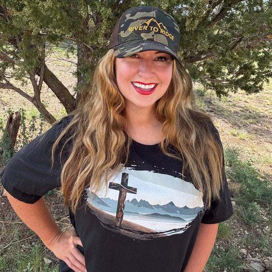 Woman wearing a black t-shirt with a mountain design and a cap outdoors.
