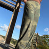 Person wearing green patterned pants standing on a concrete surface with a wooden bench and trees in the background.