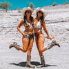Two women in cowboy hats and boots posing on a rocky landscape.