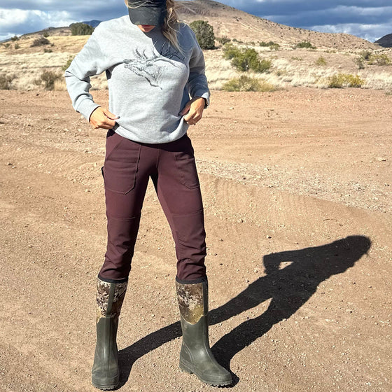 pretty woman standing on dirt road wearing elk sweatshirt, hat and work pants and camo rubber boots
