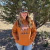 Person wearing an orange hoodie with a deer graphic and camouflage cap standing in a natural setting.