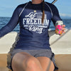Person wearing a navy blue shirt with 'Let Freedom Ring' text, sitting on a boat with ocean view.