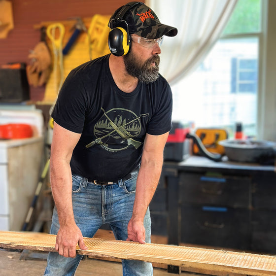 Man doing lumber / woodwork wearing a black hunting and fishing logo t shirt from River to Ridge Clothing Brand and ear and eye protection