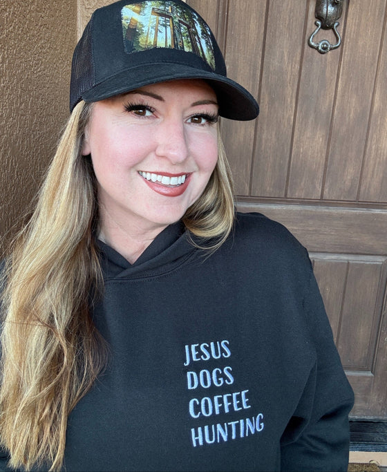 Woman wearing a black cap and black hoodie with text, standing in front of a wooden door.