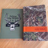 Two books on a wooden surface, one with a green cover and deer illustration, the other with a camouflage cover and orange band labeled 'HOLY BIBLE'.