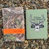 Two books on a bed of small stones, one with camouflage design and 'HOLY BIBLE' text, the other with deer design and 'Follow the WORD Not the herd' text.