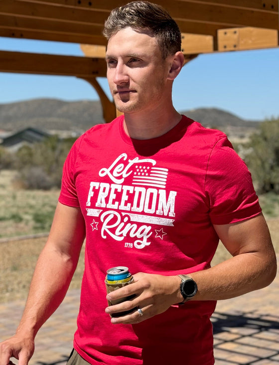 Man at a BBQ wearing a Let Freedom Ring, patriotic red T shirt and holding a beer - shirt from River to Ridge Clothing Brand