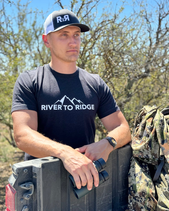 River to Ridge log t shirt in black and white on a guy standing by a 4 wheeler outdoors