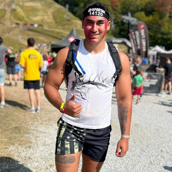 Man at  Spartan Obstacle Race wearing Mens Gym Shorts with Camo American Flag Pattern from River to Ridge Clothing Brand and also a white muscle tank top with an elk on it