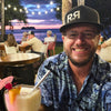 Man with a cocktail at an outdoor setting with people and a sunset.