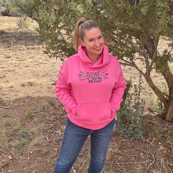 Person wearing a pink hoodie with 'Stay Wild' text, standing outdoors.