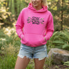 Woman wearing a pink 'Stay Wild' hoodie in a forest setting