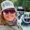 Person wearing a 'Stay Wild' cap and sunglasses with boats and a truck in the background.