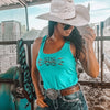 Woman in turquoise tank top with 'Stay Wild' text, white cowboy hat, and sunglasses in a barn setting.