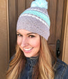 Woman wearing a striped knit beanie with a pom-pom in front of a wooden door.