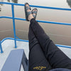 Person wearing sandals and black pants with a brand logo, sitting on a boat with a lake view.
