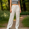 Woman standing on a wooden path in a forest wearing a gray top and white patterned pants.