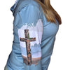 Person wearing a light blue shirt with a cross design on the back, standing against a wooden door.