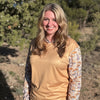 Woman wearing a beige long-sleeve shirt with nature-themed sleeves outdoors.