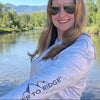 Woman wearing sunglasses and a long-sleeve shirt with 'River to Ridge' logo outdoors.