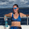 Woman in blue athletic wear holding a water bottle on a boat with ocean and sky background
