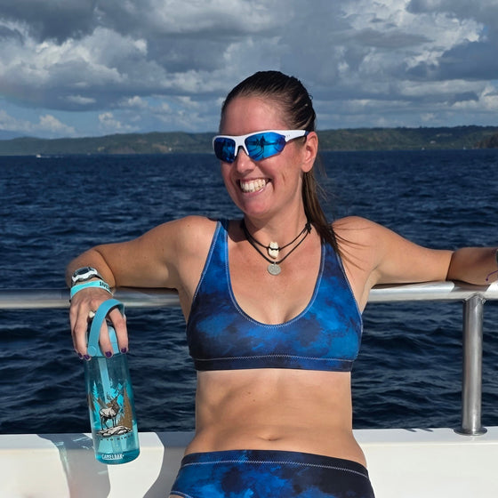 Woman in blue athletic wear holding a water bottle on a boat with ocean and sky background
