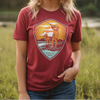 Woman wearing a red t-shirt with a graphic design in a field during sunset