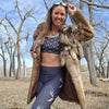 Woman in outdoor setting wearing a fur coat, sports bra, and leggings with deer design.