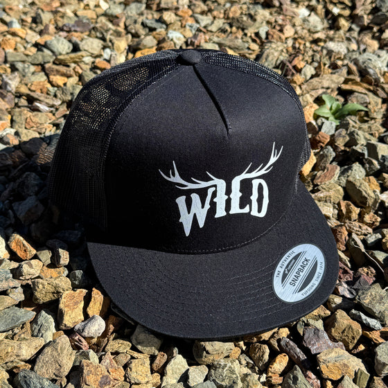Black cap with 'WILD' and deer antlers on a gravel surface
