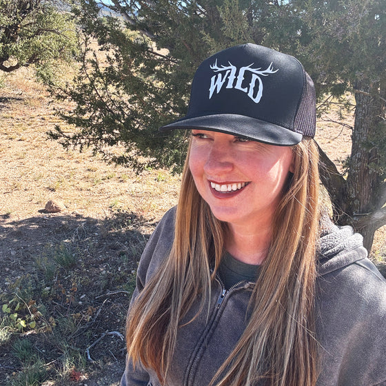 Person wearing a black cap with 'WILD' printed on it, standing outdoors in a natural setting.