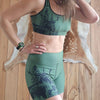 Person wearing a green sports bra and shorts set with nature-themed design on a wooden floor.