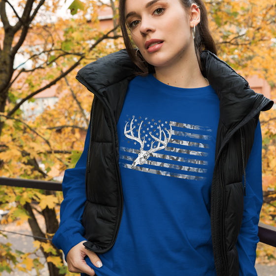 Woman wearing a whitetail deer skull flag logo in camo on a blue long sleeve t shirt from river to ridge clothing brand with a black vest, outdoors in the fall