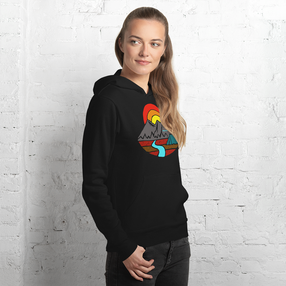 Woman wearing a hoodie from River to Ridge Brand in black by a brick wall and it says mountain air feeds my soul with a mountain a river and a tent on it