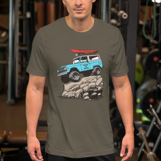 man at the gym wearing a t shirt. Mens offroad classic T shirt in army green, with a graphic of a bronco in blue doing a rock crawl with a kayak on top. From the Brand River to Ridge