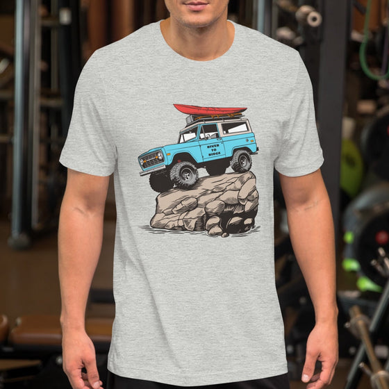 man at the gym wearing a t shirt. Mens offroad classic T shirt in grey, with a graphic of a bronco in blue doing a rock crawl with a kayak on top. From the Brand River to Ridge