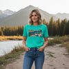 Turquoise t-shirt with a graphic of a lakeside scene on a white background